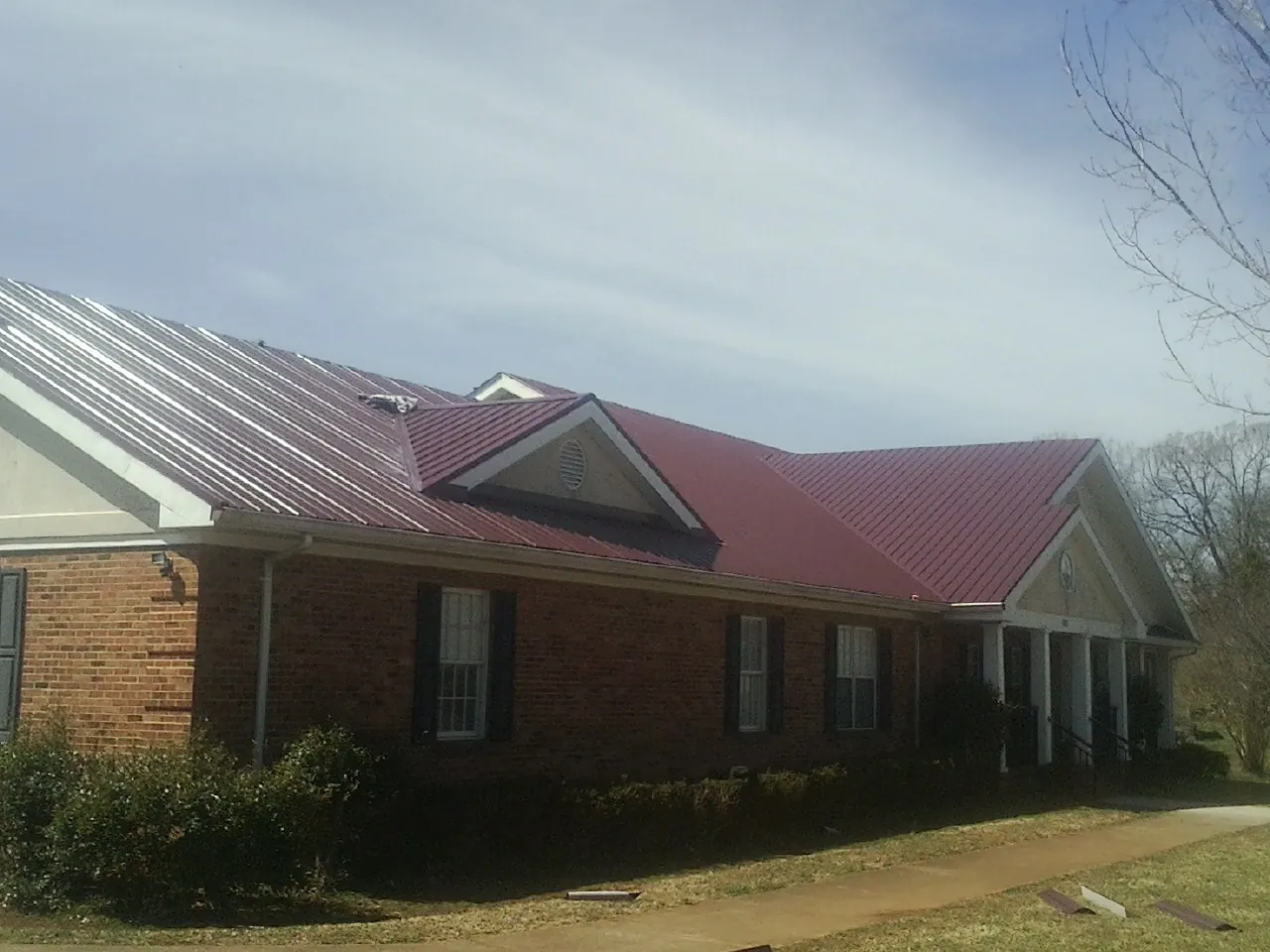 Red metal roof with gabled entries on a long brick building, from a Hail Damage Roof Repair job in North Chicago