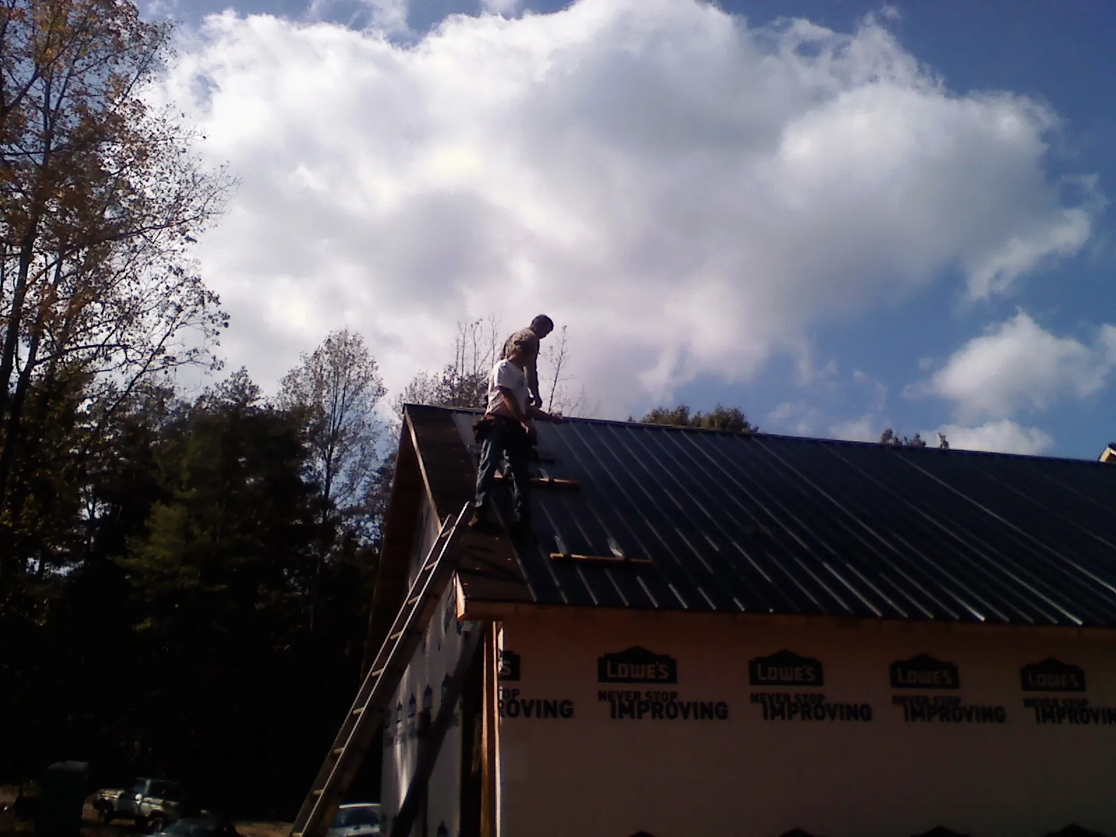 Roofer fastening dark metal panels high against a cloudy sky, from a Roof Inspection job in North Chicago