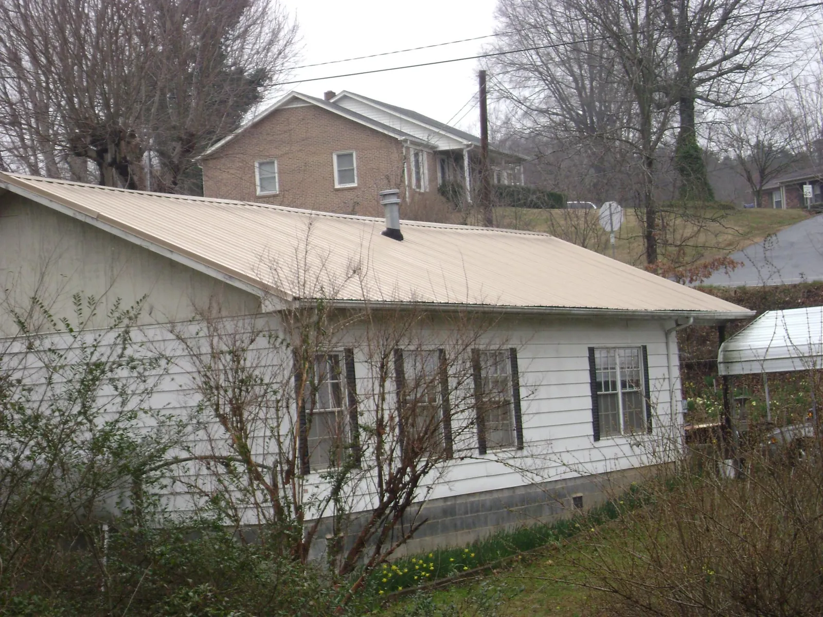 Tan metal roof on a white sided house set into a hillside — Commercial Roofing by Roofing Brothers in North Chicago